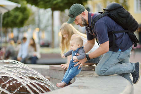 Father holding his infant son by city fountain. Young dad playing with his baby boy son. Family having fun with water on hot summer day.の写真素材