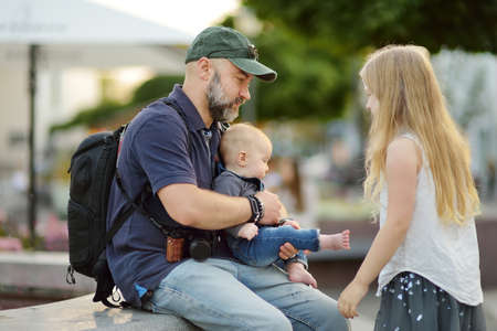Father holding his infant son by city fountain. Young dad playing with his baby boy and his older daughter. Family having fun with water on hot summer day.の写真素材