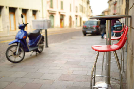Empty small outdoor restaurant tables and red chairs in the city of Bergamo, Italyの写真素材