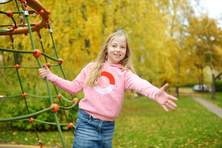 Pretty young girl having fun on a playground in beautiful autumn park. Cute preteen child playing outdoors in late autumn. Outdoor activities for family with kids.の写真素材