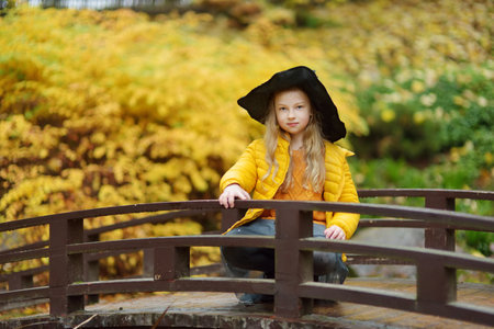 Cute young girl wearing black witch hat having fun outdoors. Kid trick or treating on Halloween. Family time at Thanksgiving and Halloween. Festive season in October.の写真素材