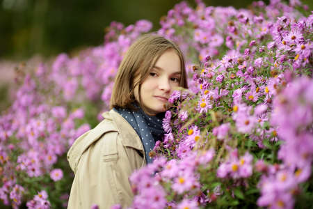 Portrait of teen girl with different shades of purple chrysantemum flowers in a backyard garden in autumn. Fall season. Decorative flowers outdoors.の写真素材