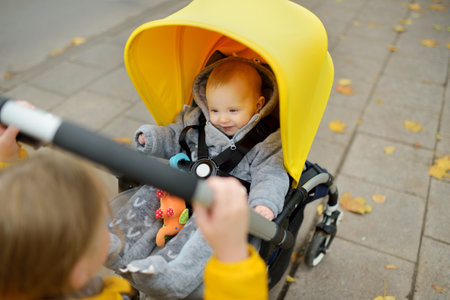 Sweet baby boy wearing warm clothes sitting in a stroller outdoors. Little child in pram. Infant kid in pushchair. Autumn walks with kids. Family leisure with little child.の写真素材
