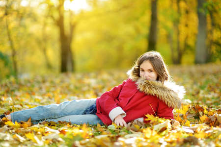 Adorable young girl having fun on beautiful autumn day. Happy child playing in autumn park. Kid gathering yellow fall foliage. Autumn activities for children.の写真素材