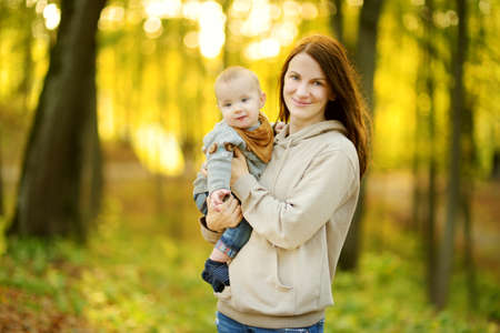 Cute little baby boy in his mothers arms. Mom and son having fun on sunny autumn day in city park. Adorable son being held by his mommy.の写真素材