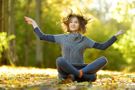 Adorable young girl having fun on beautiful autumn day. Happy child playing in autumn park. Kid gathering yellow fall foliage. Autumn activities for children.の写真素材