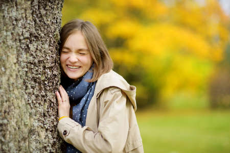 Adorable young girl having fun on beautiful autumn day. Happy child playing in autumn park. Kid gathering yellow fall foliage. Autumn activities for children.の写真素材