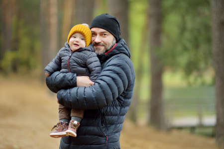 Cute little baby boy in his fathers arms. Dad and son having fun on cold autumn day in city park. Adorable son being held by his daddy.の写真素材