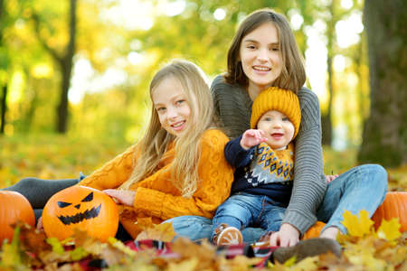 Two cute young girls and their baby brother holding a small pumpkin with painted scary face on sunny autumn day. Kids trick or treating on Halloween. Family time at Halloween.の写真素材