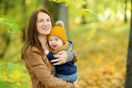 Cute little baby boy in his mothers arms. Mom and son having fun on sunny autumn day in city park....