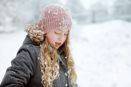 Adorable young girl having fun in beautiful winter park during snowfall. Cute child playing in a...