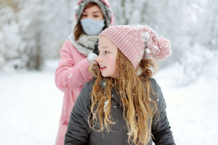 Two adorable young girls having fun together in beautiful winter park. Cute sisters playing in a snow. Winter activities for family with kids.の写真素材