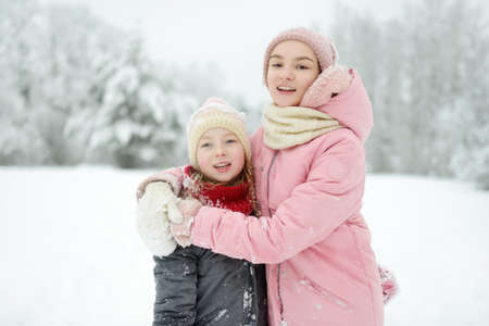 Two adorable young girls having fun together in beautiful winter park. Cute sisters playing in a snow. Winter activities for family with kids.の写真素材