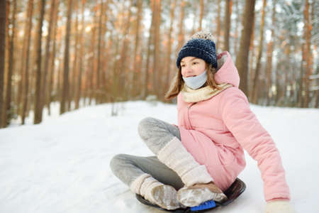 Funny young girl having fun with a sleigh in beautiful winter park. Cute child playing in a snow. Winter activities for kids.の写真素材