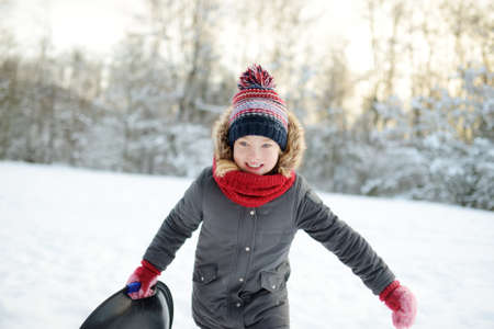 Adorable young girl having fun in beautiful winter park during snowfall. Cute child playing in a...