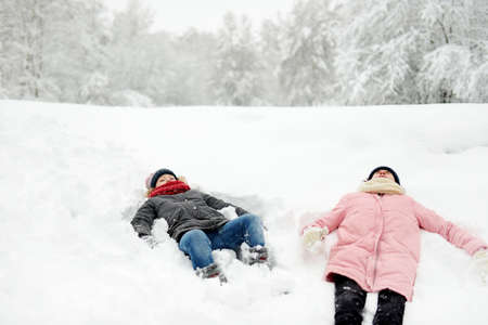 Two adorable young girls having fun together in beautiful winter park. Cute sisters playing in a snow. Winter activities for family with kids.の写真素材