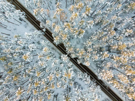 Beautiful aerial view of snow covered pine forests and a road winding among trees. Rime ice and hoar...