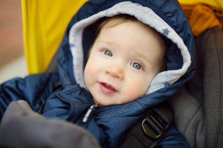 Sweet baby boy wearing warm clothes sitting in a stroller outdoors. Little child in pram. Infant kid in pushchair. Winter walks with kids. Family leisure with little child.の写真素材