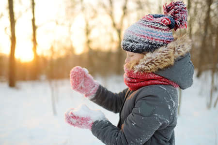 Adorable young girl having fun in beautiful winter park during snowfall. Cute child playing in a snow. Winter activities for family with kids.の写真素材