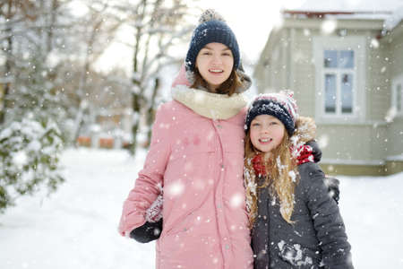Two adorable young girls having fun together in beautiful winter park. Cute sisters playing in a snow. Winter activities for family with kids.の写真素材