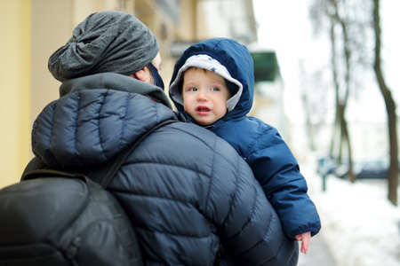 Cute little baby boy in his fathers arms. Dad and son having fun on chilly winter day in city park....