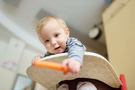 Cute little baby boy eating carrot sitting in a white highchair. Introducing first solid foods. Fresh organic vegetables for infants. Healthy nutrition for family with kids.の写真素材
