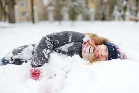 Adorable young girl having fun in beautiful winter park during snowfall. Cute child playing in a snow. Winter activities for family with kids.の写真素材