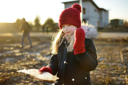 Happy young girl playing with thin ice puddles formed on the frozen soil in winter. Child having fun in winter. Winter activities for kids.の写真素材
