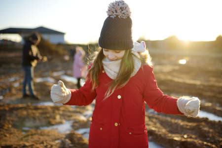 Group of children playing with thin ice puddles formed on the frozen soil in winter. Kids having fun...