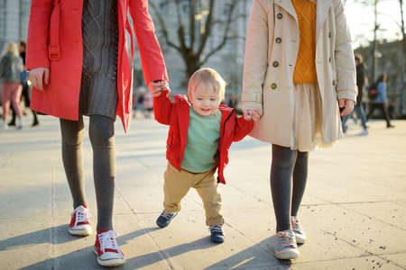 Two big sisters and their baby brother having fun outdoors. Two young girls holding their baby boy sibling on sunny spring day. Kids with large age gap. Kids during city walk.の写真素材