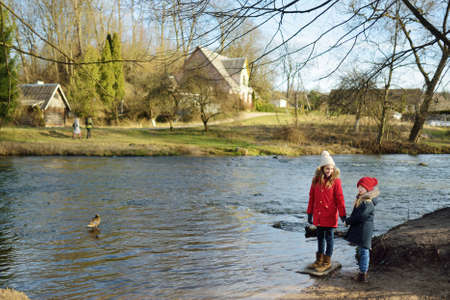 Two cute young sisters having fun by a river on warm spring day. Children playing together by a water. Outdoor family activities in early spring.の写真素材