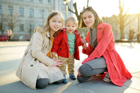 Two big sisters and their baby brother having fun outdoors. Two young girls holding their baby boy sibling on sunny spring day. Kids with large age gap. Kids during city walk.の写真素材