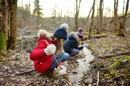 Two cute young sisters having fun by a river on warm spring day. Children playing together by a...