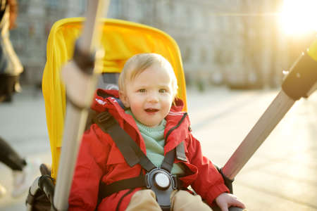 Sweet baby boy wearing red jacket sitting in a stroller outdoors. Little child in pram. Infant kid...