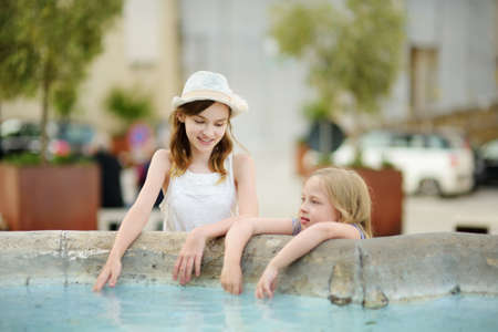 Young girls playing in a fountain of Pitigliano town, located atop a volcanic tufa ridge. Beautiful italian towns and villages. Etruscan heritage, Grosseto, Tuscany, Italy.の写真素材