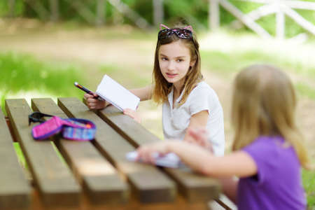 Two happy sisters drawing together at the wooden table outdoors. Little girls sketching outside on beautiful summer day. Summer activities for children.の写真素材