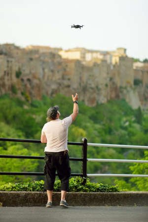 A man launching a drone near Pitigliano town, located atop a volcanic tufa ridge. Taking pictures frome the above. Digital photography using drones. Etruscan heritage, Grosseto, Tuscany, Italy.の写真素材