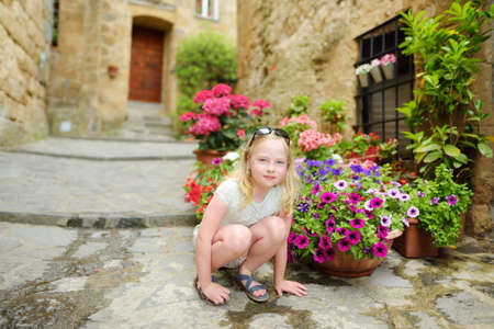 Little girl exploring old medieval streets of famous Civita di Bagnoregio village, located on top of a volcanic tuff hill overlooking the Tiber river valley, Lazio, Italyの写真素材