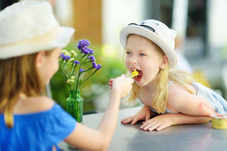 Two little sisters having an ice-cream on warm and sunny summer day during family vacations in Orvieto, Umbria Italy. Cute children sitting in outdoor cafe and eating a gelato.の写真素材
