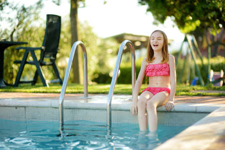 Cute young girl having fun in outdoor pool. Child learning to swim. Kid having fun with water toys. Family fun in a pool. Summer activities for the family with kids.の写真素材