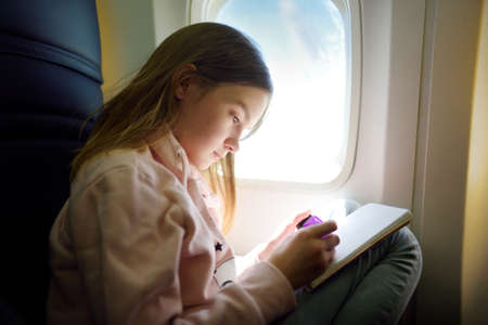 Adorable young girl traveling by an airplane. Child sitting by aircraft window and drawing a picture with colorful pencils. Traveling abroad with kids.の写真素材