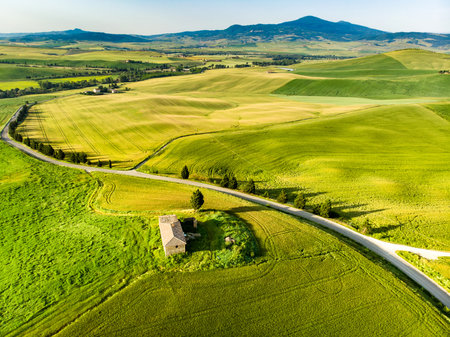 Stunning aerial view of green fields and farmlands with small villages on the horizon. Summer rural landscape of rolling hills, curved roads and cypresses of Tuscany, Italy.の写真素材