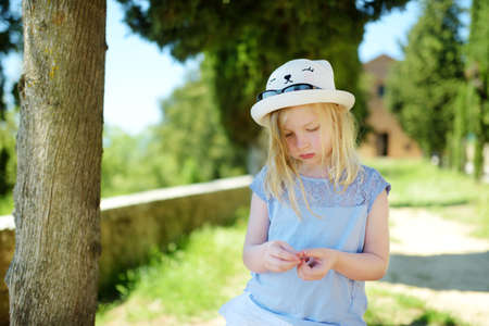 Young girl admiring the view of green fields and farmlands with small villages on the horizon. Summer rural landscape of rolling hills surrounding Pienza town, Tuscany, Italy.の写真素材