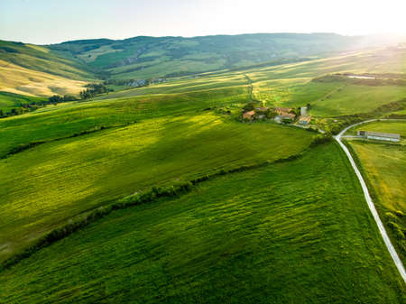 Stunning aerial view of green fields and farmlands with small villages on the horizon. Summer rural landscape of rolling hills, curved roads and cypresses of Tuscany, Italy.の写真素材