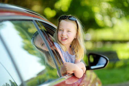 Funny young girl sticking her head out the car window looking forward for a roadtrip or travel. Family car travel with kids.の写真素材