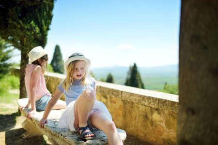 Two sisters admiring the view of green fields and farmlands with small villages on the horizon. Summer rural landscape of rolling hills surrounding Pienza town, Tuscany, Italy.の写真素材