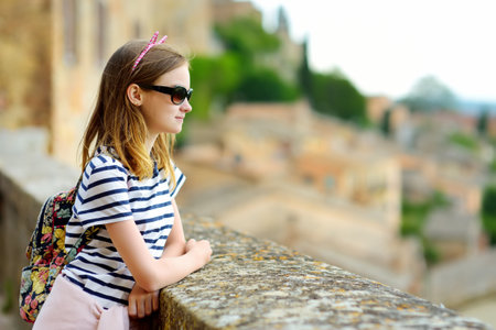 Young girl enjoying the view of green hills and pastures of Tuscany and rooftops of Montepulciano town, located on top of a limestone ridge surrounded by vineyards. Tuscany, Italy.の写真素材
