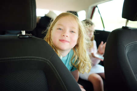 Funny young girls sitting in the car looking forward for a roadtrip or travel. Family car travel with kids.の写真素材