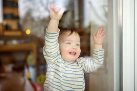Adorable toddler boy looking through the window at home. Little child looking outside.の写真素材