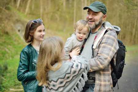 Young father and his three kids hiking in the woods. Family of four having fun on a walking trail on...